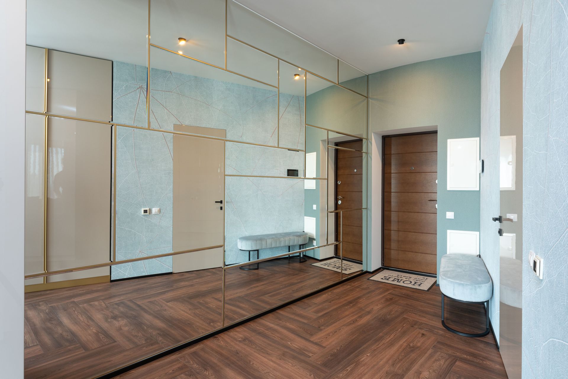 Spacious hallway with entrance door and big wardrobe with mirror and reflection of doors placed in modern apartment with pouf