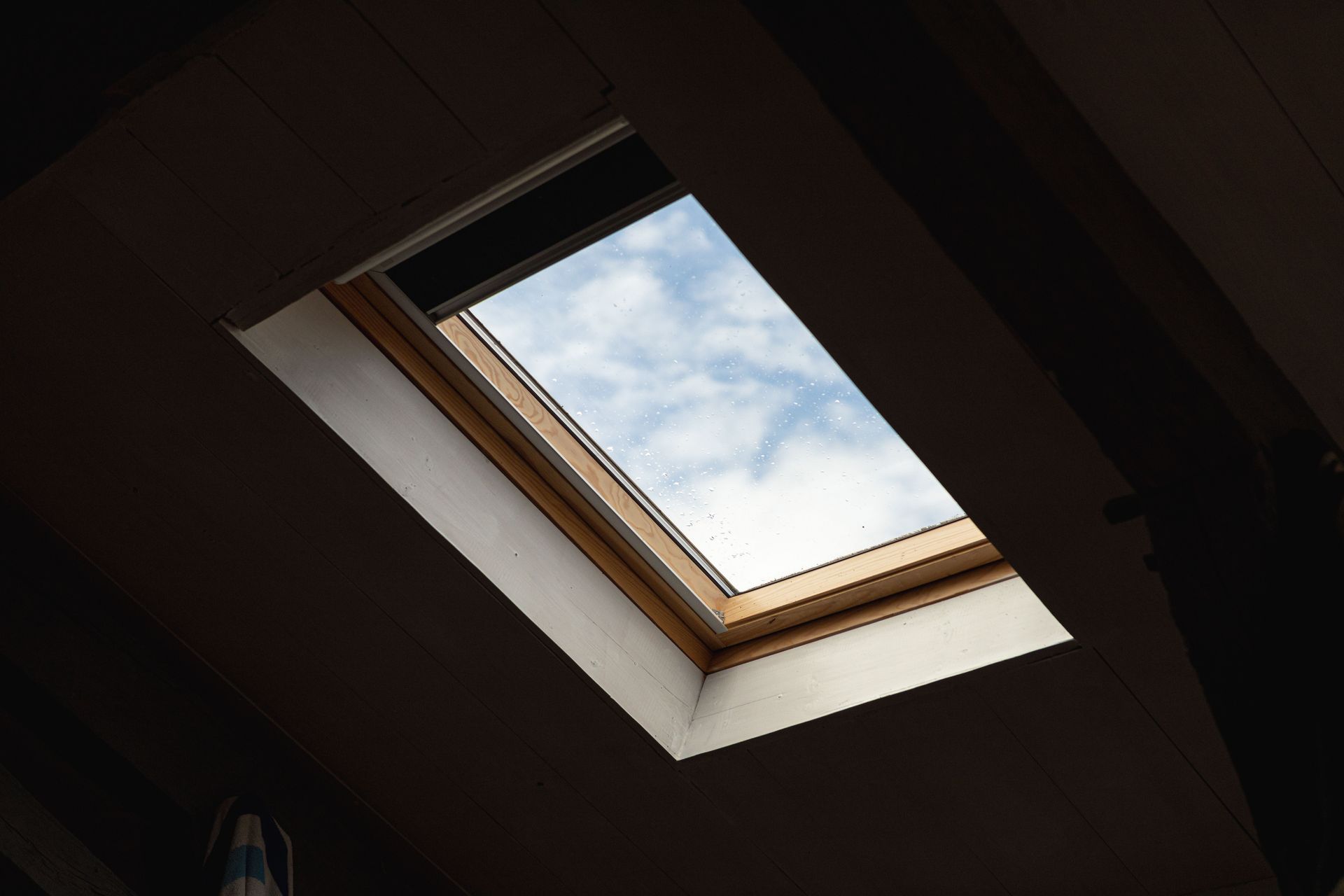A skylight in a dark room providing a view of a cloudy sky, adding natural light.