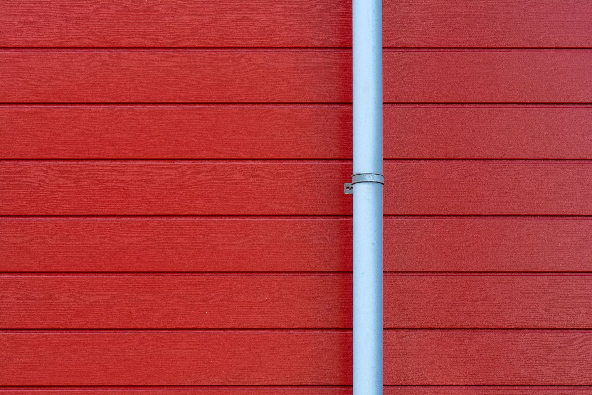 A minimalist photo of a red wall with a white rain gutter, showing clean lines and vibrant color contrast.